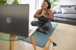 © Alessandro Biascioli - African young woman doing yoga virtual fitness class with laptop at home - E-learning and people wellness lifestyle concept