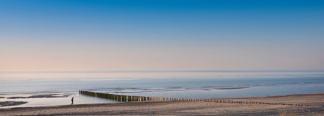 lonely figure strolls along beach of north sea in dutch province of Zeeland under blue sky in spring