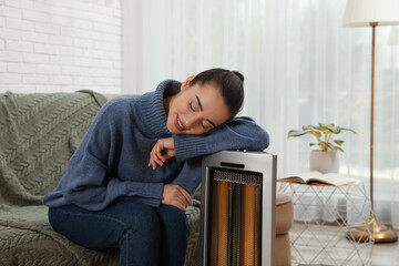 Wall Mural - Young woman getting warm near electric heater at home