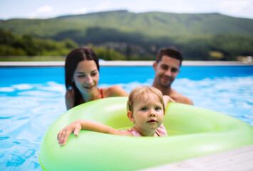 Young family with small daughter in swimming pool outdoors in backyard garden.