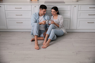 Happy couple sitting on warm floor in kitchen. Heating system