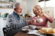 © JustLife - Senior couple eating breakfast in the kitchen. Husband and wife talking and laughing while eating a sandwich