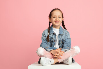 Wall Mural - Happy kid, girl isolated on pink studio background. Looks happy, cheerful, sincere. Copyspace. Childhood, education, emotions concept