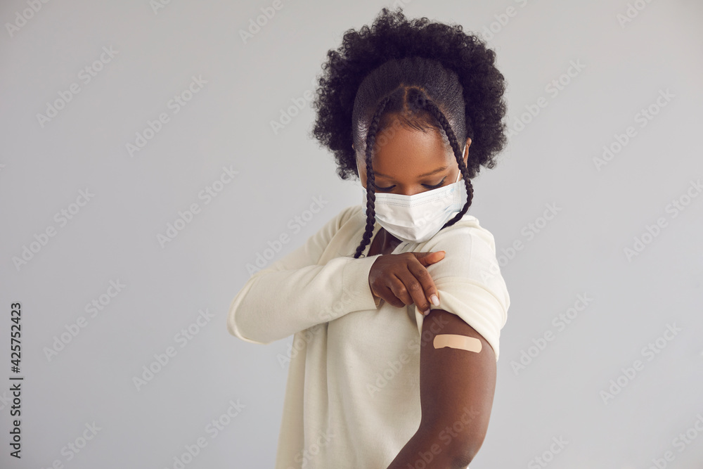 Woman receives Covid 19 vaccine injection. Young black lady showing arm with adhesive plaster bandage after getting vaccinated for coronavirus. Vaccination concept, light gray copy space background - obrazy, fototapety, plakaty 