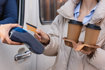 partial view of woman with credit card and coffee to go near courier holding payment terminal