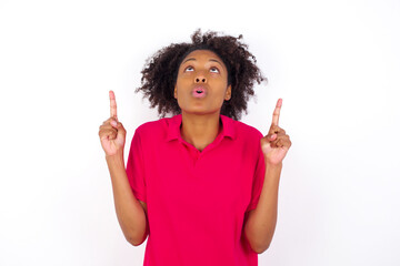 Wall Mural - young beautiful African American woman wearing pink t-shirt against white wall being amazed and surprised looking and pointing up with fingers showing something strange.