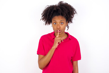Wall Mural - young beautiful African American woman wearing pink t-shirt against white wall makes hush gesture, asks be quiet. Don't tell my secret or not speak too loud, please!