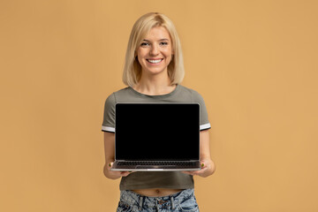 Useful website. Cheerful woman holding laptop computer, showing blank screen to camera over colorful studio wall, mockup