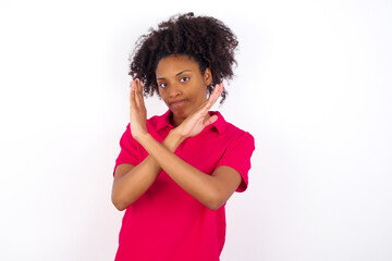 Wall Mural - young beautiful African American woman wearing pink t-shirt against white wall Has rejection angry expression on face and crossing hands doing refusal negative sign.