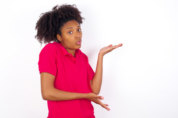 Wall Mural - young beautiful African American woman wearing pink t-shirt against white wall pointing aside with both hands showing something strange and saying: I don't know what is this. Advertisement concept.