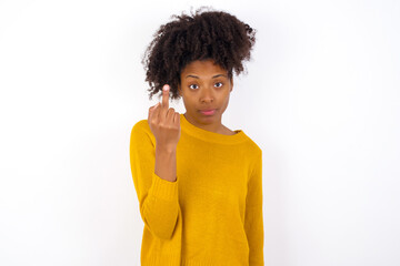 Wall Mural - young beautiful African American woman wearing yellow sweater against white wall shows middle finger bad sign asks not to bother. Provocation and rude attitude.