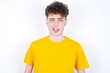 Coquettish young caucasian handsome man with curly hair wearing yellow T-shirt against white studio background  smiling happily, blinking at camera in a playful manner, flirting with you.