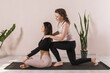 The teacher of universal yoga performs the straightening of the spine of a student sitting on a mat in the lotus position against the wall, a technique for improving posture