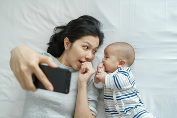 Wall Mural - Young mother and newborn baby taking selfie with mobile phone on bed.