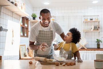 Wall Mural - Cheerful smiling Black son enjoying playing with his father while doing bakery at home. Playful African family having fun cooking baking cake or cookies in kitchen together.