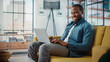 © Gorodenkoff - Handsome Black African American Man Working on Laptop Computer while Sitting on a Sofa in Cozy Living Room. Freelancer Working From Home. Browsing Internet, Using Social Networks, Having Fun in Flat.