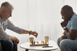 © Prostock-studio - Concentrated senior man playing chess with friend, sitting at table