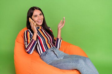 Poster - Profile side view portrait of attractive cheerful girl sitting in chair talking on phone isolated over bright green color background