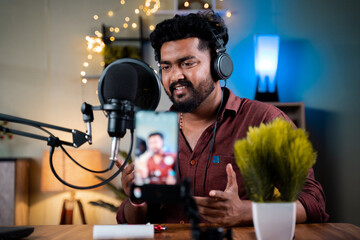 Young social media influencer recording his podcast on mobile phone - concept of vlogging, content creation from home office.