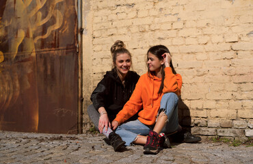 Two teenage skater girls are hanging out in the neighborhood, chatting and smiling.