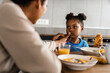 © Drobot Dean - Black mother and daughter having breakfast at home kitchen