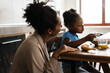 Black mother and daughter having breakfast at home kitchen