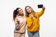 © F8  \ Suport Ukraine - Portrait of a two women making selfie photo on smartphone while showing two fingers sign on gray background