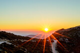 Fototapeta Góry - Beautiful Sunset over the Mountains of Crete Island, Greece. Panoramic View from a Mountain Top with a Dirt Road. Golden Sun Rays.