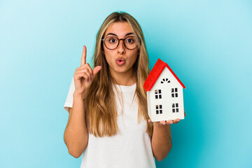 Young caucasian woman holding a house model isolated on blue background having some great idea, concept of creativity.