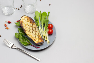 Grilled baked eggplant on gray plate with tomatoes and greens. Fork and two glasses.