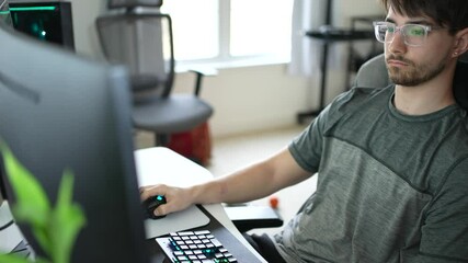 Front closeup view of young hip businessman in casual attire working on keyboard and widescreen computer in home office.