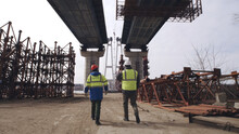 Unrecognizable Contractors Walking Under Bridge