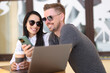 © H_Ko - Smiling man and woman in sunglasses communicate in coffee near laptop