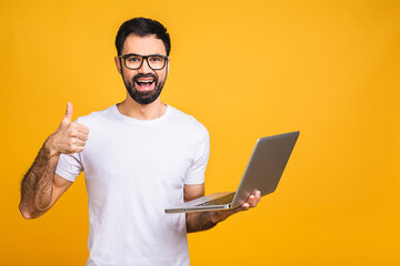 Wall Mural - Confident business expert. Confident young handsome man in casual holding laptop and smiling while standing isolated over yellow background. Thumbs up.