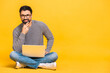 © denis_vermenko - Portrait of a happy young bearded man in casual holding laptop computer while sitting on a floor isolated over yellow background.