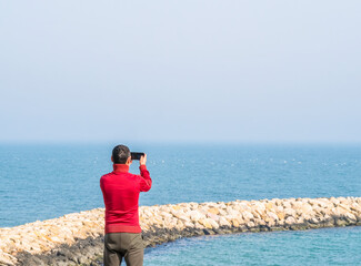 Tourist taking a picture with his smartphone at the edge of the Black Sea in Constanta, Romania.