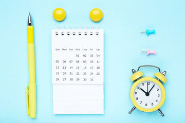 Wall Mural - Calendar page with alarm clock and pen on blue background