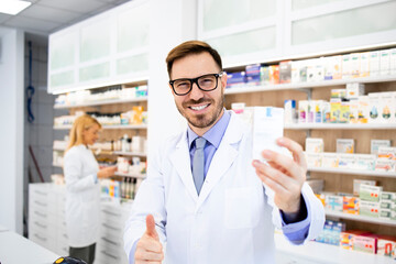 Wall Mural - Portrait of smiling caucasian pharmacist holding vitamins in drug store.