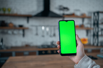 closeup of female hand using smartphone with green screen mockup at home kitchen