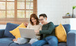 © NaMong Productions - Asian couple man and woman watching movie in computer laptop together on sofa in living room at home. family lifestyle concept.