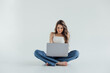 © ALEXSTUDIO - Portrait of a smiling casual girl holding laptop computer while sitting on a floor isolated over white background