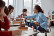 © Ivan - Young teacher helps to read her student. Elementary school kids sitting on desks and reading books in classroom