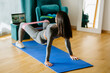 © shevtsovy - Fit young Pacific Islander woman fitness training at home. Attractive female athlete working out for wellbeing in domestic gym, training legs muscles doing glutes booty exercise with resistance band.