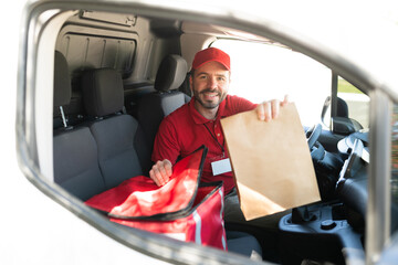 Wall Mural - Cheerful delivery driver giving a bag with fast food to a customer