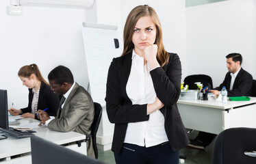 Wall Mural - Portrait of frustrated young business woman in coworking space with working colleagues behind