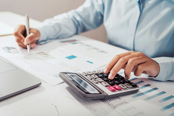 Fototapete - Woman accountant use calculator and computer with holding pen on desk in office. finance and accounting concept