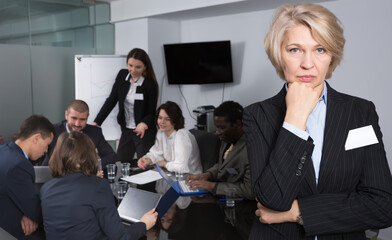 Wall Mural - Unhappy mature business woman standing in meeting room on background with coworkers.