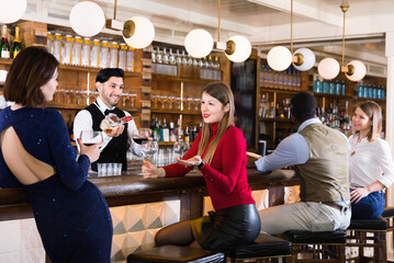 Portrait of positive smiling barman and happy cheerful glad people who are standing near bar counter in luxurious restaurant.