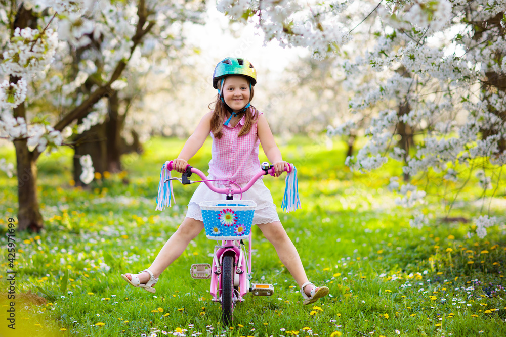 Kids on bike in spring park. Girl riding bicycle. - obrazy, fototapety, plakaty 