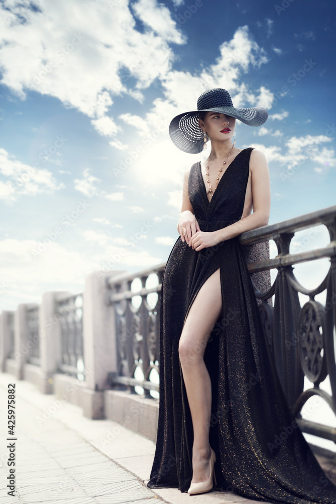 Fashion Woman in Hat and Black Dress Outdoor. Elegant Lady in Summer Hat  long Evening Gown